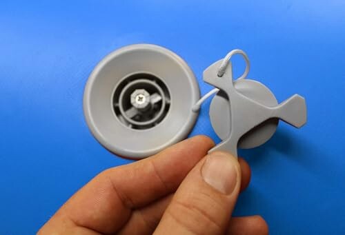 Hand holding a gray suction cup with hook against blue background