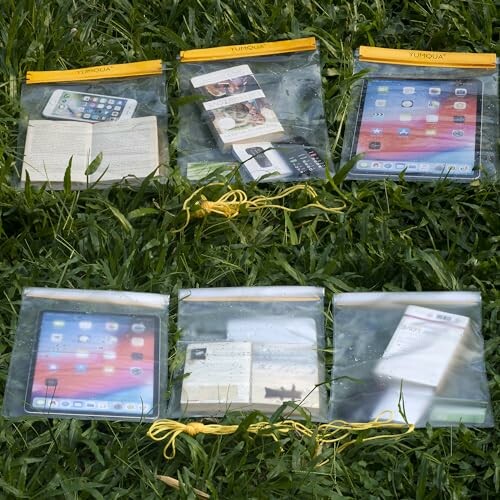 Transparent waterproof bags holding electronic devices and a book on grass.